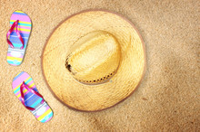 Top View Of Straw Hat And Flip Flops On Beach Sand