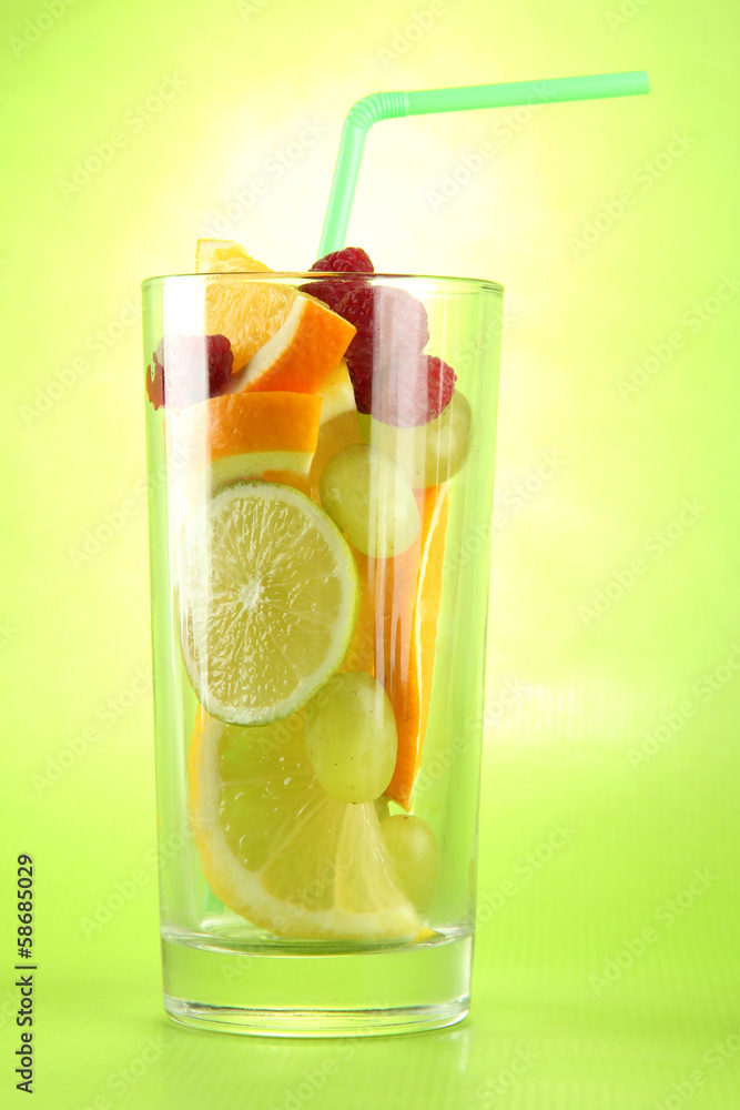 transparent glass with citrus fruits, on green background