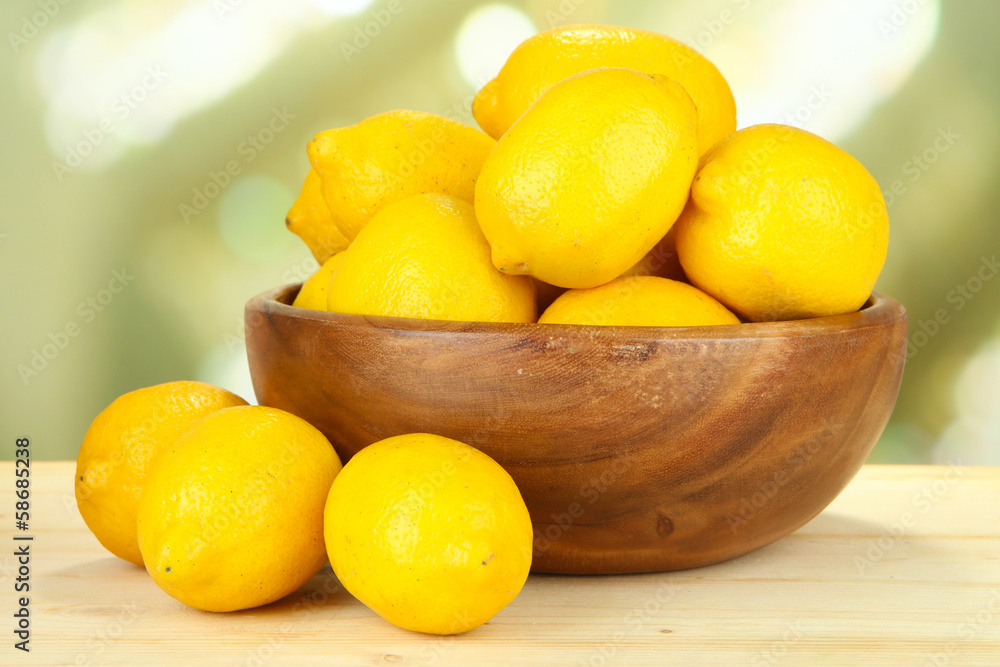Ripe lemons in bowl on table on bright background