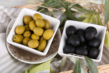 Olives in bowls with branch on napkin in basket close-up