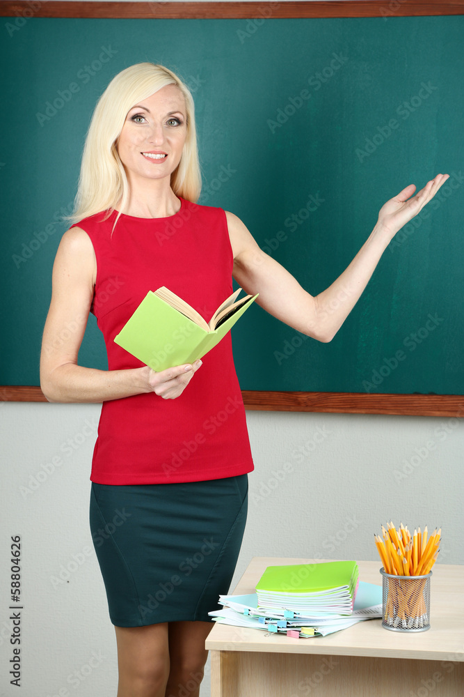 School teacher near table on blackboard background