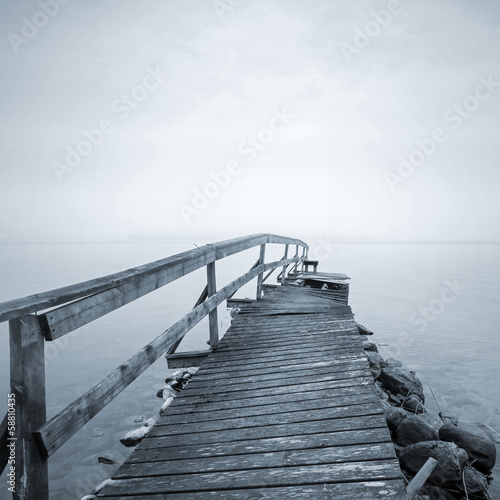Fototapeta na wymiar Old ruined wooden pier perspective on the lake in foggy morning