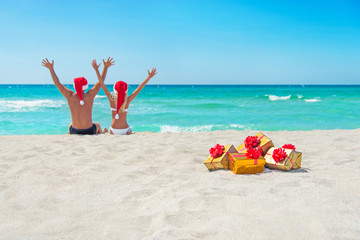 Wall Mural - happy couple in santa hats hands up at sea beach with christmas