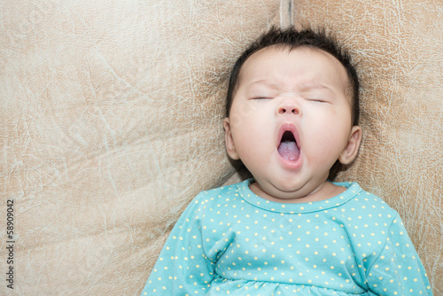 Fototapeta Portrait of a yawning baby girl on a leather background