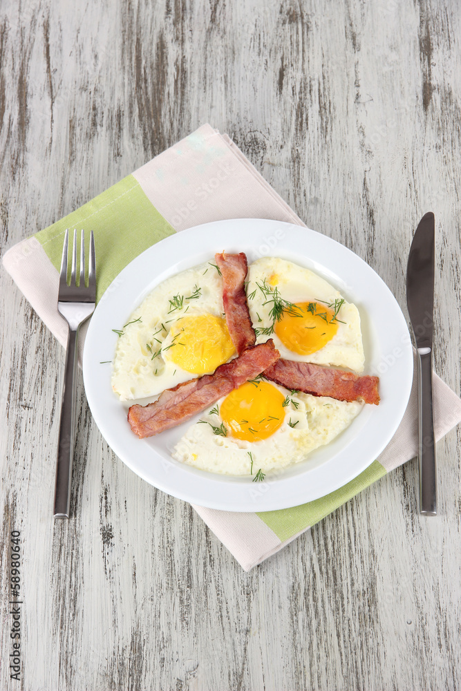 Scrambled eggs and bacon on plate on napkin on wooden table
