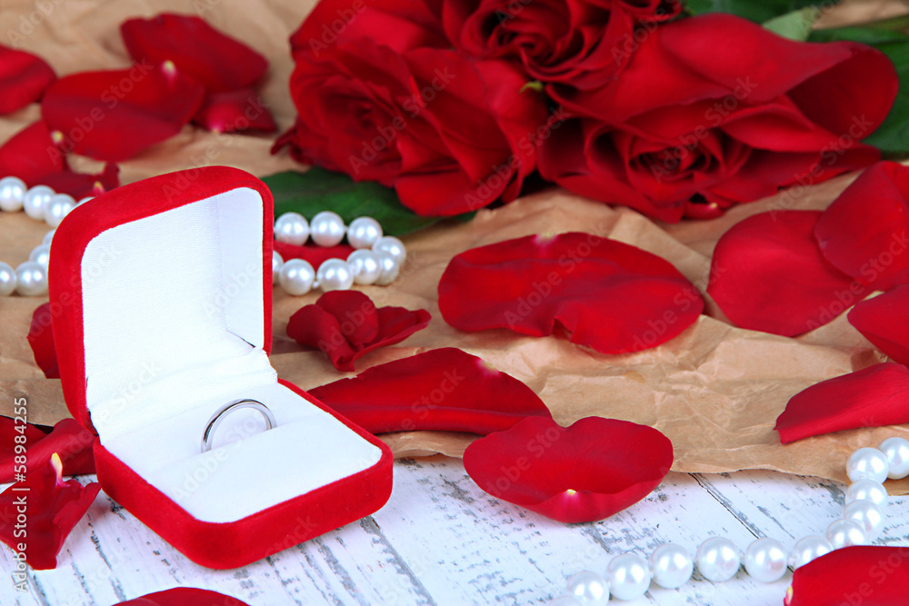 Ring surrounded by roses and petals on wooden table close-up
