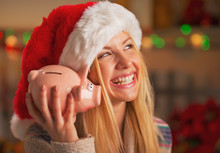 Smiling Teenage Girl In Santa Hat Shaking Piggy Bank