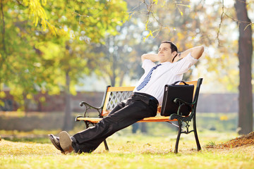 Wall Mural - Young businessperson sitting on a bench and relaxing in a park