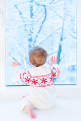 Wall Mural - Little baby sitting at a window watching snow covered trees