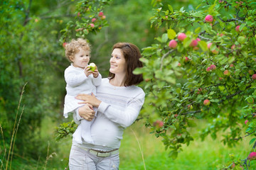 Wall Mural - Young pregnant woman and her baby daughter under appletree