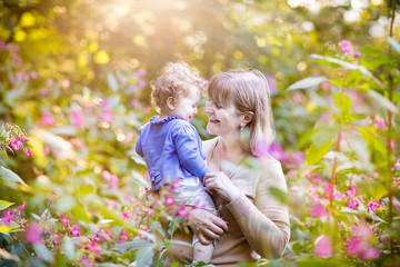 Wall Mural - Beautiful woman with a happy baby girl in a garden at sunset