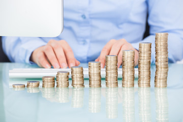 Coins Stacked On Desk In Front Of Businesswoman