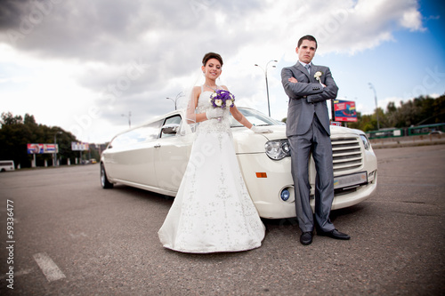 Photographie Young just married couple standing against long white limousine