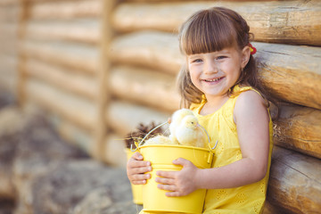 Happy little girl with a basket of small chickens sitting outdoo