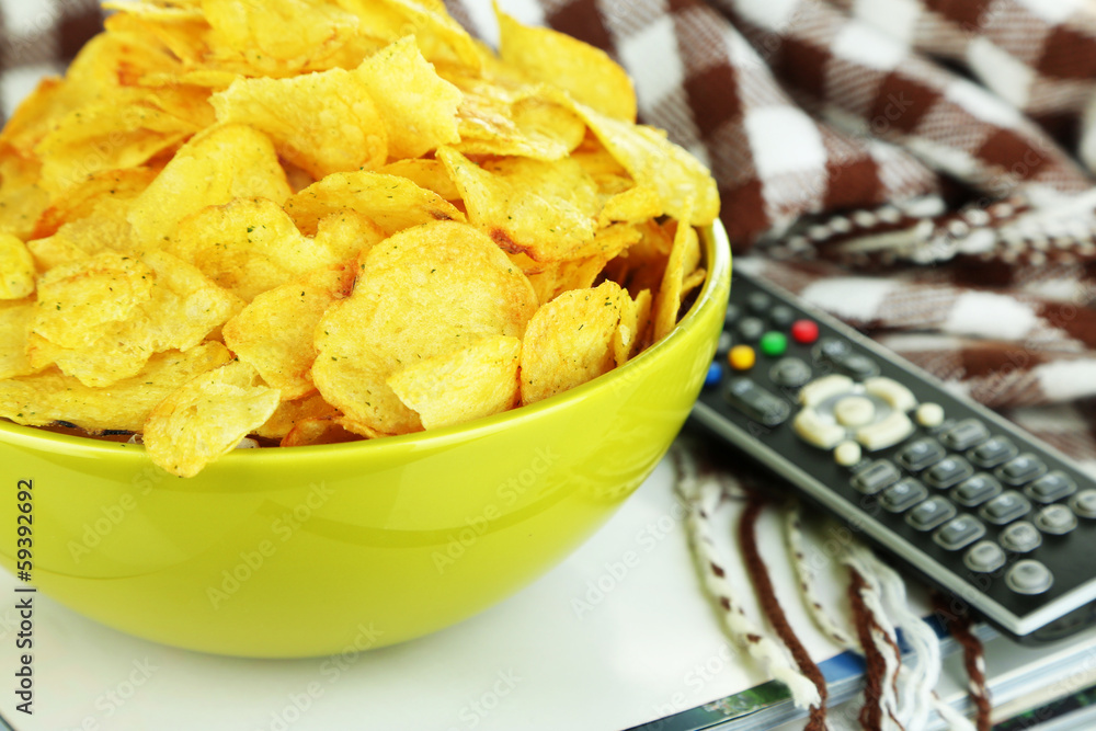 Chips in bowl, magazines, plaid and TV remote close-up