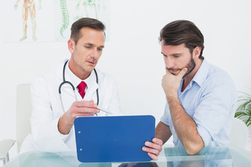 Male doctor discussing reports with patient at desk