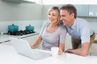 © lightwavemedia - Happy couple using laptop in kitchen