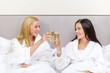 © Syda Productions - smiling girlfriends with champagne glasses in bed