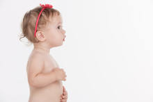 Cute Little Baby Girl With Red  Band Standing In Profile.