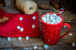 Red knitted mug filled with hot chocolate and marshmallows on wo