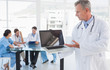 © WavebreakMediaMicro - Doctor holding laptop with group around table in hospital