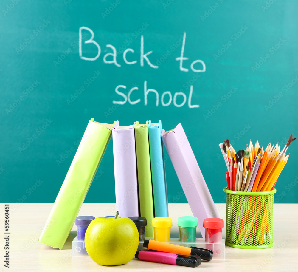 School supplies on table on blackboard background