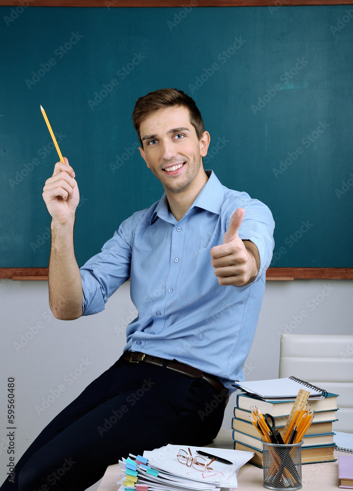 Young teacher sitting on desk in school classroom