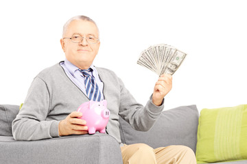 Poster - Senior gentleman seated on a sofa with a piggy bank and dollars