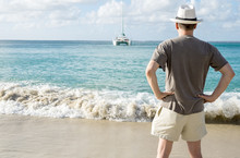 Back View Of A Man On A Beach Looking At A Catamaran