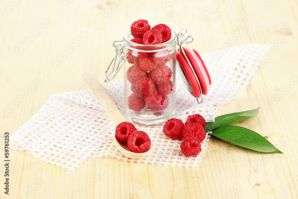 Ripe raspberries in bank on wooden table close-up