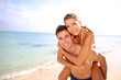 © goodluz - Man giving piggyback ride to girlfriend at the beach