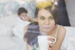 © MDBPIXS - Thougtful woman having coffee at home with man lying in background