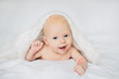 © Svetlana Iakusheva - Happy baby lying on white bed under soft blanket, smiling and looking at camera