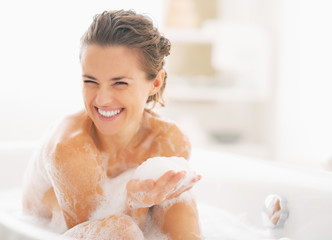 portrait of happy young woman playing with foam in bathtub