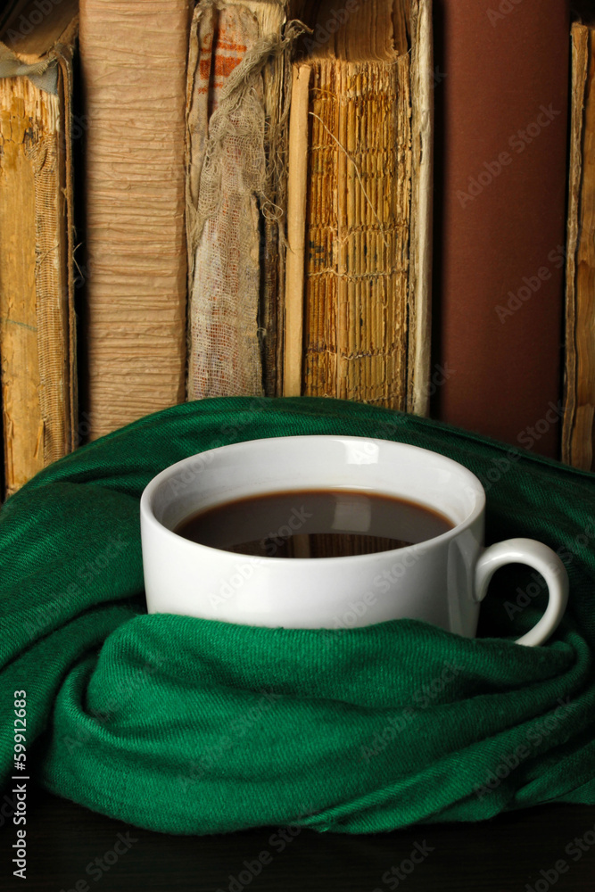 Cup of coffee wrapped in scarf on books background