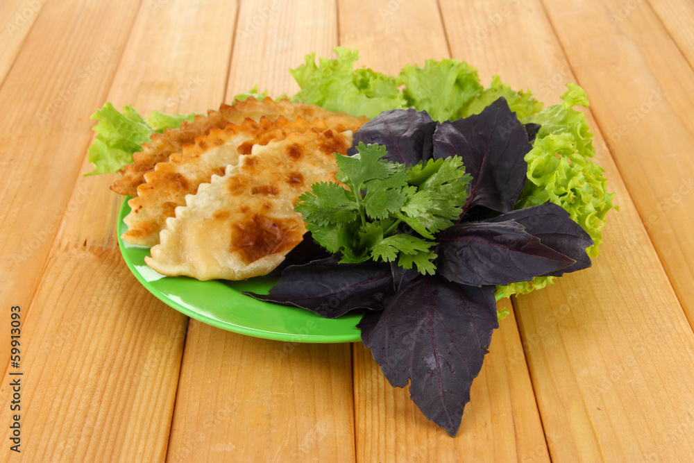 Tasty chebureks with fresh herbs on plate,on wooden background