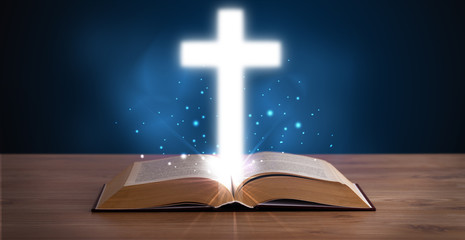 Open holy bible with glowing cross in the middle