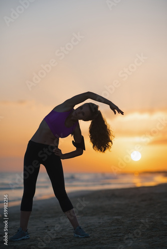 Plakat na zamówienie Silhouette of fitness young woman stretching on beach at dusk