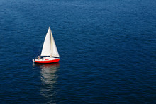 A Lone White Sail Of A Red Sailboat On A Calm Blue Sea