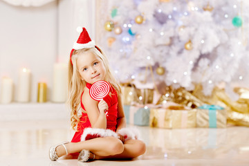 Beautiful little Santa girl near the Christmas tree.  Happy girl