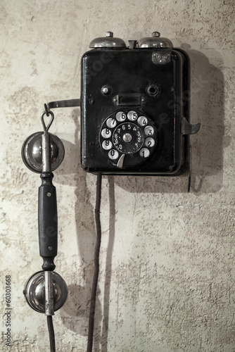 Fototapeta na wymiar Vintage black phone hanging on old gray concrete wall
