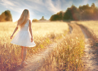 happy girl on the road in a wheat field at sunset