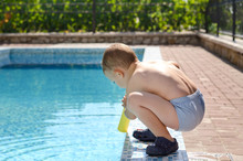 Young Boy Playing At The Edge Of A Swimming Pool