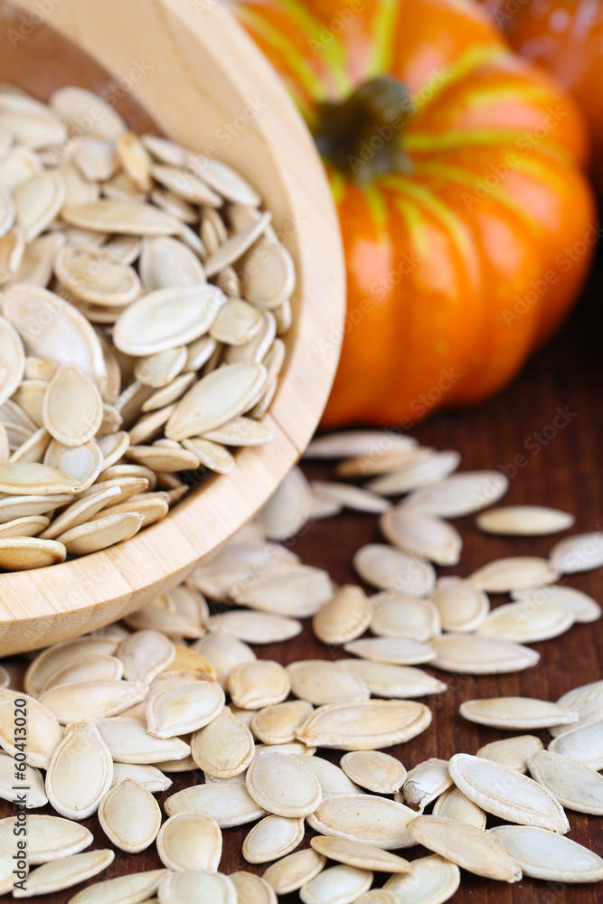 Pumpkin seeds in bowl with pumpkin on table close up