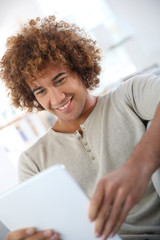 Wall Mural - Cheerful mixed-raced guy websurfing on tablet