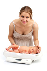 Young Caucasian mother and her newborn baby on a weight scale