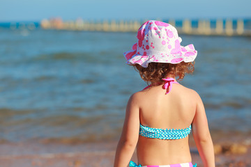 Kid girl standing on seashore and looking on blue sea