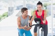 © WavebreakMediaMicro - Woman with male instructor working out at spinning class