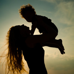 Wall Mural - Mother and little son silhouettes on beach at sunset