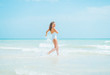 © Alliance - Smiling young woman in swimsuit running into sea